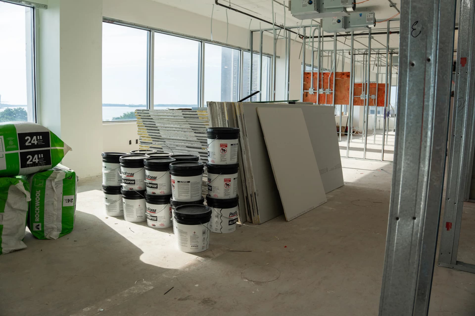 Drywall sheets, joint compound and insulation staged beside windows at 100 Biscayne